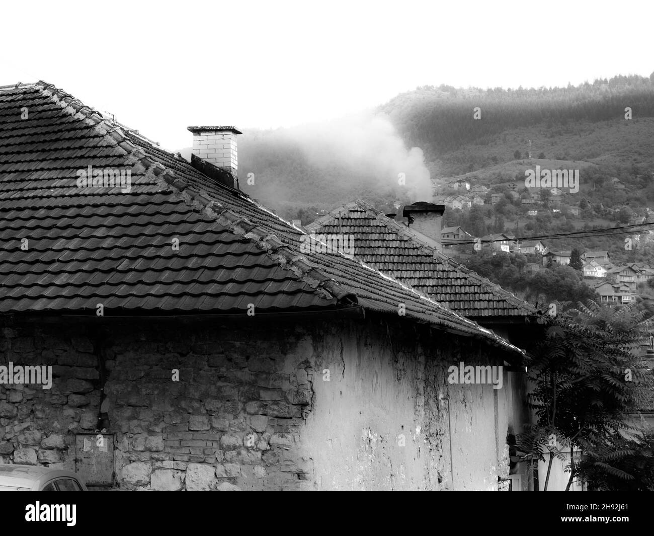 Grayscale shot of an old metallic roof and smoke coming out of chimneys. Stock Photo