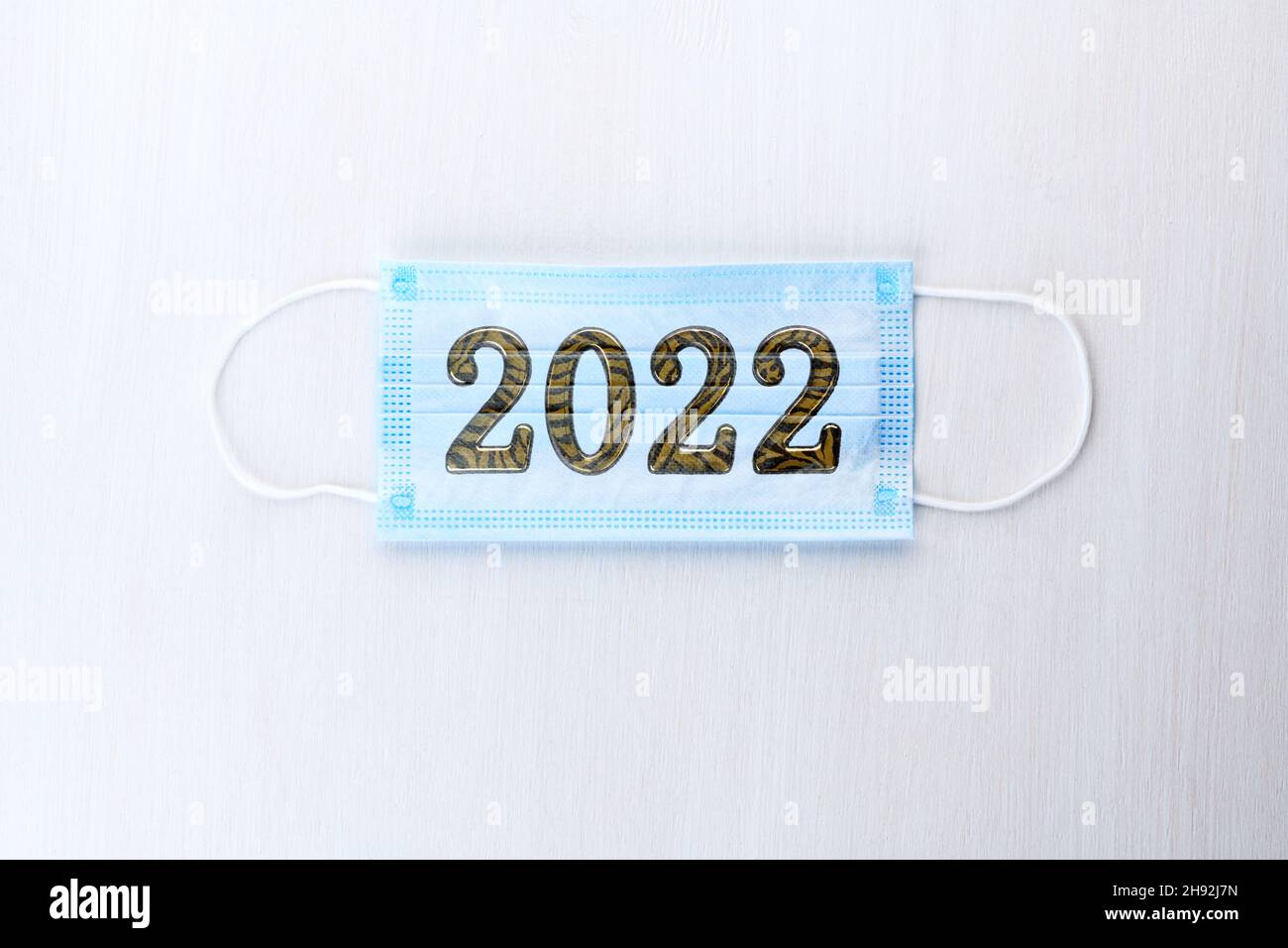 Medical mask with numbers 2022 Tiger on white wooden background. Coronavirus infection control concept. Symbol 2022 Tiger Stock Photo