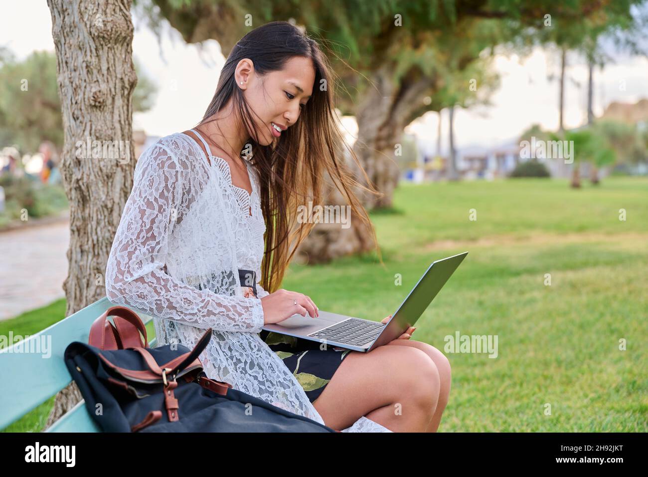 Beautiful young Asian woman using laptop sitting on an outdoor bench ...