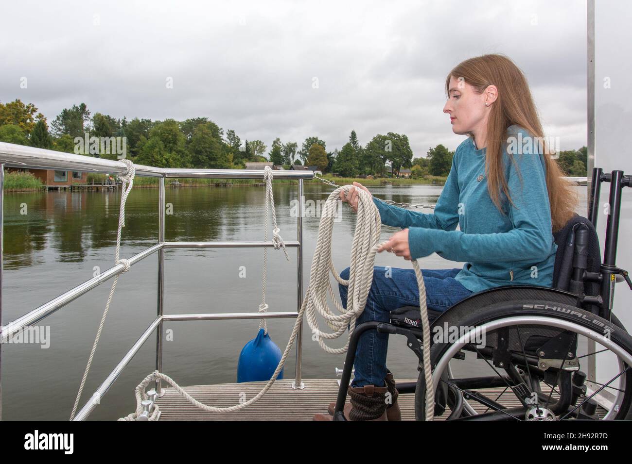 Frau im Rollstuhl auf Hausboot legt die Leine zusammen Stock Photo