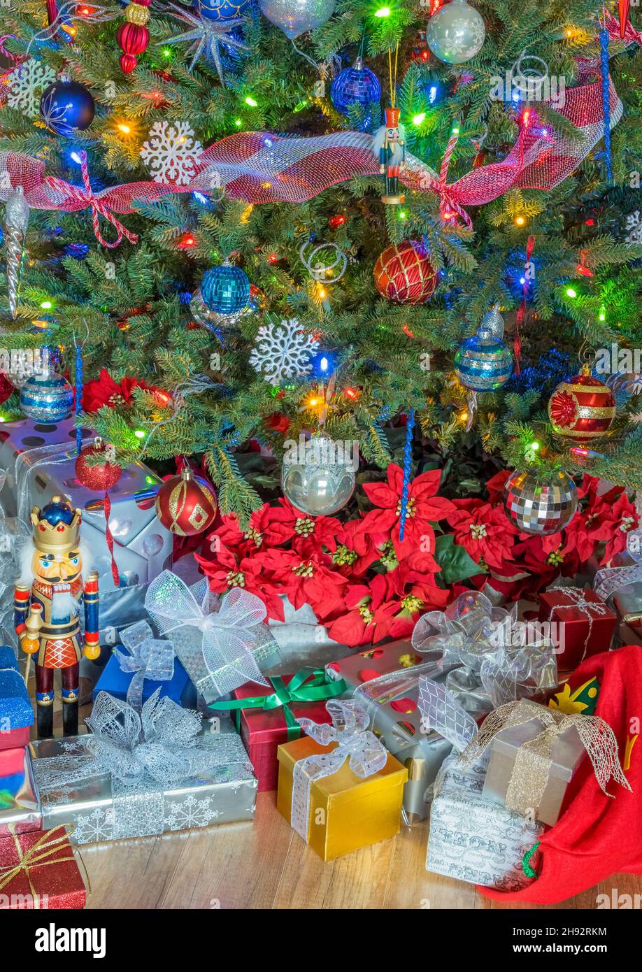 Red, white and blue decorations fill a Christmas tree and a pile of Christmas packages with Poinsettias sit under it's branches. A nutcracker guards i Stock Photo