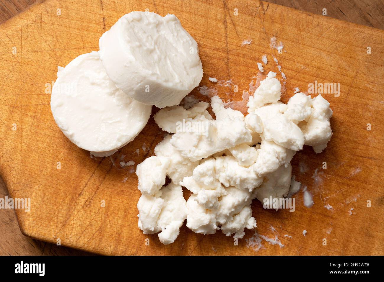 Two rounds of goat cheese and crumbled goat cheese on wood chopping board. Top view. Stock Photo