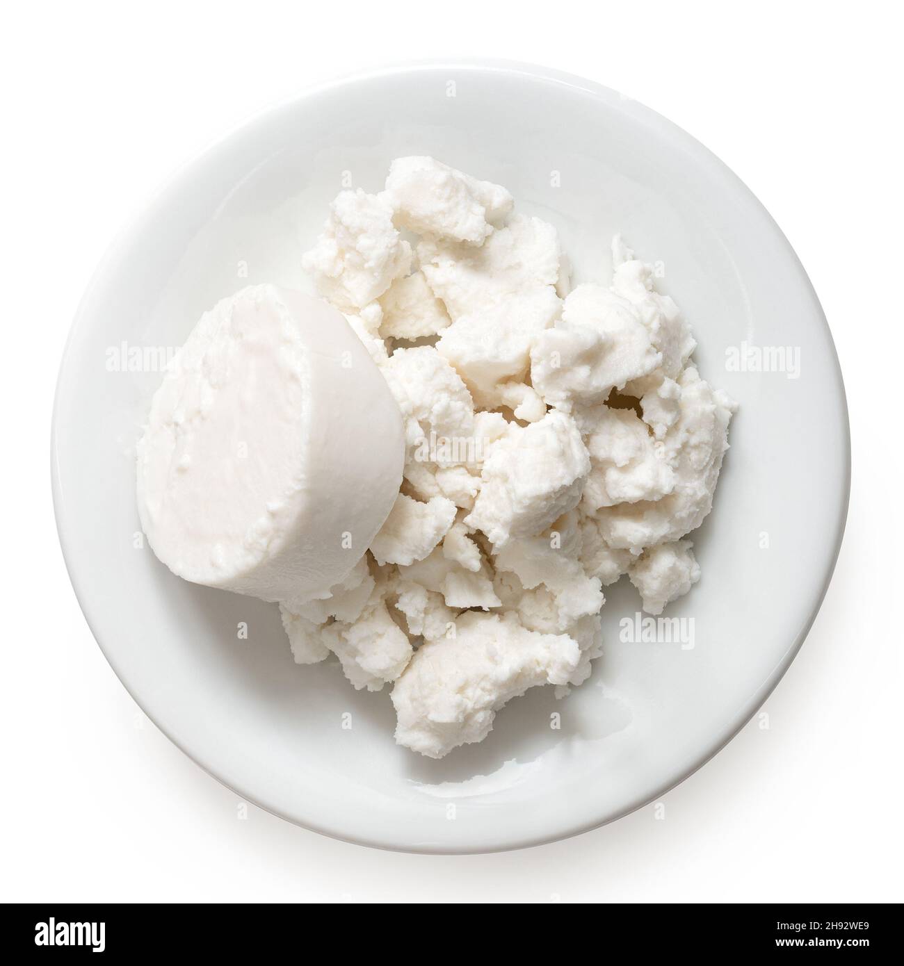 Round of goat cheese and crumbled goat cheese on white ceramic plate isolated on white. Top view. Stock Photo