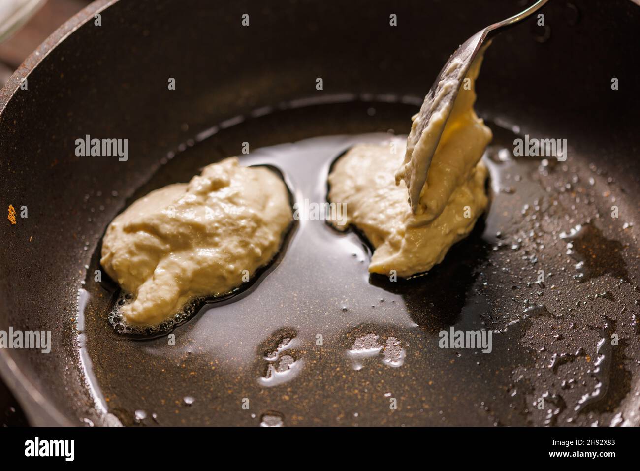 spoon puts semiliquid dough into a preheated pan covered with