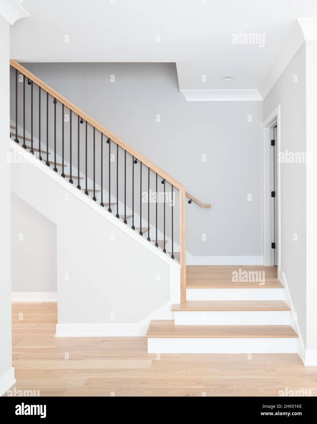 A staircase going up with natural wood steps and handrails, white risers, and wrought iron spindles. Stock Photo