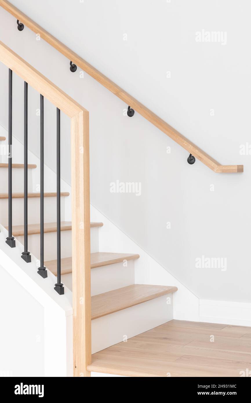A staircase going up with natural wood steps and handrails, white risers, and wrought iron spindles. Stock Photo
