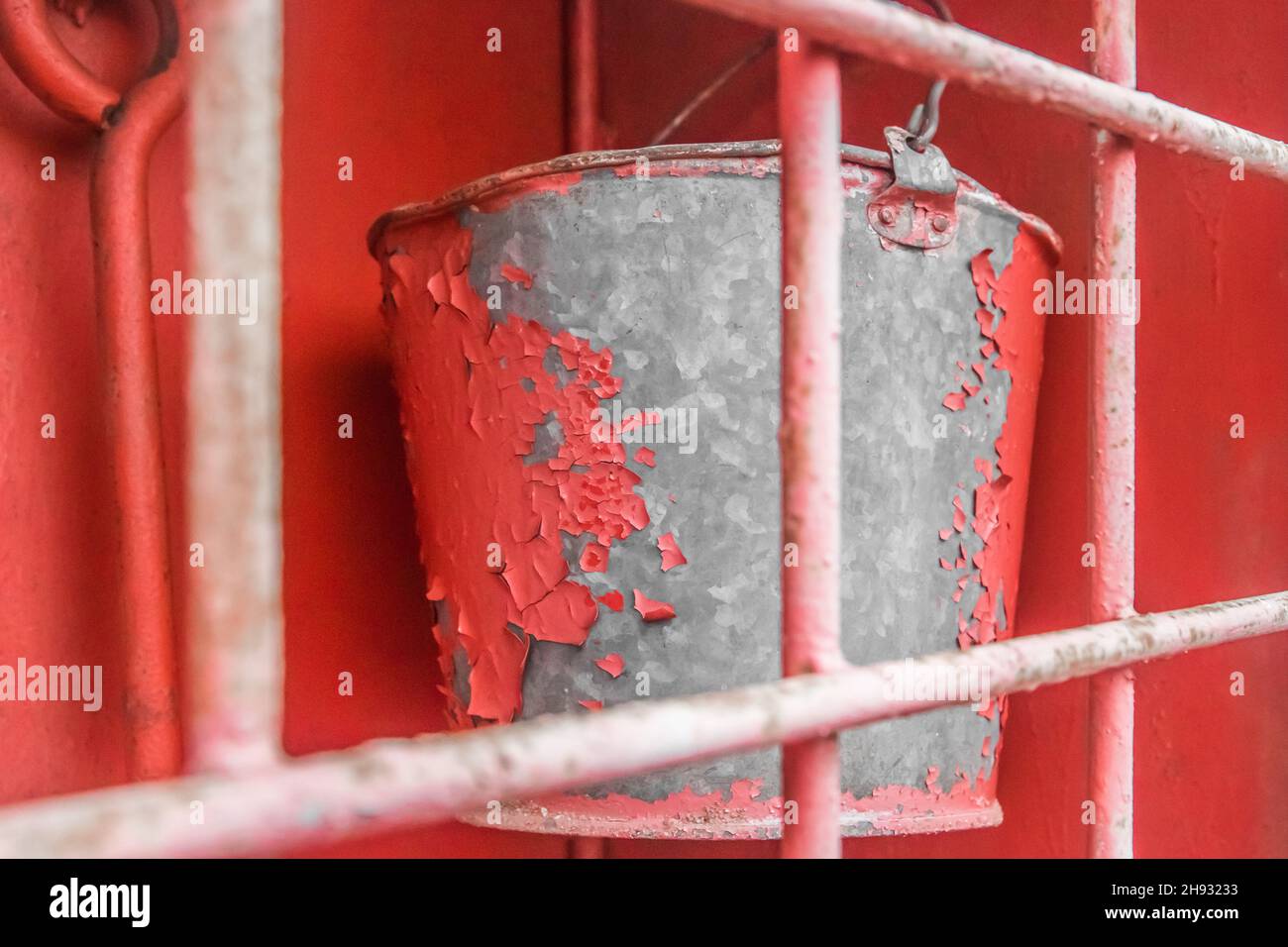A bucket of galvanized iron with red peeling paint in an old fire box equipment and tools to help in safely extinguishing a fire. Stock Photo