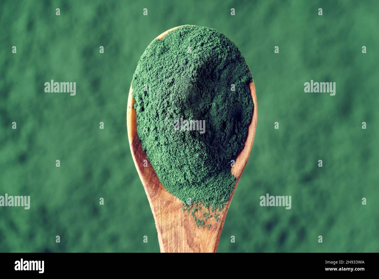 Blue green spirulina algae powder on a wooden spoon, top view. Healthy nutritional supplement