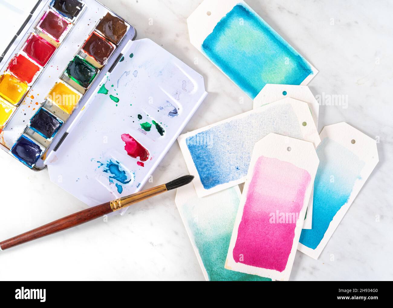Open watercolor paint box with brush painting gift tags. Stock Photo