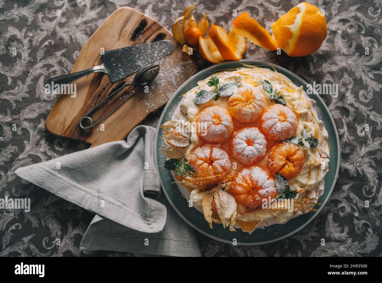 Pavlova cake low light  decorated with fresh mandarins, caramel mint physalis and poured with powder sugar meringue-based dessert named after the Russ Stock Photo