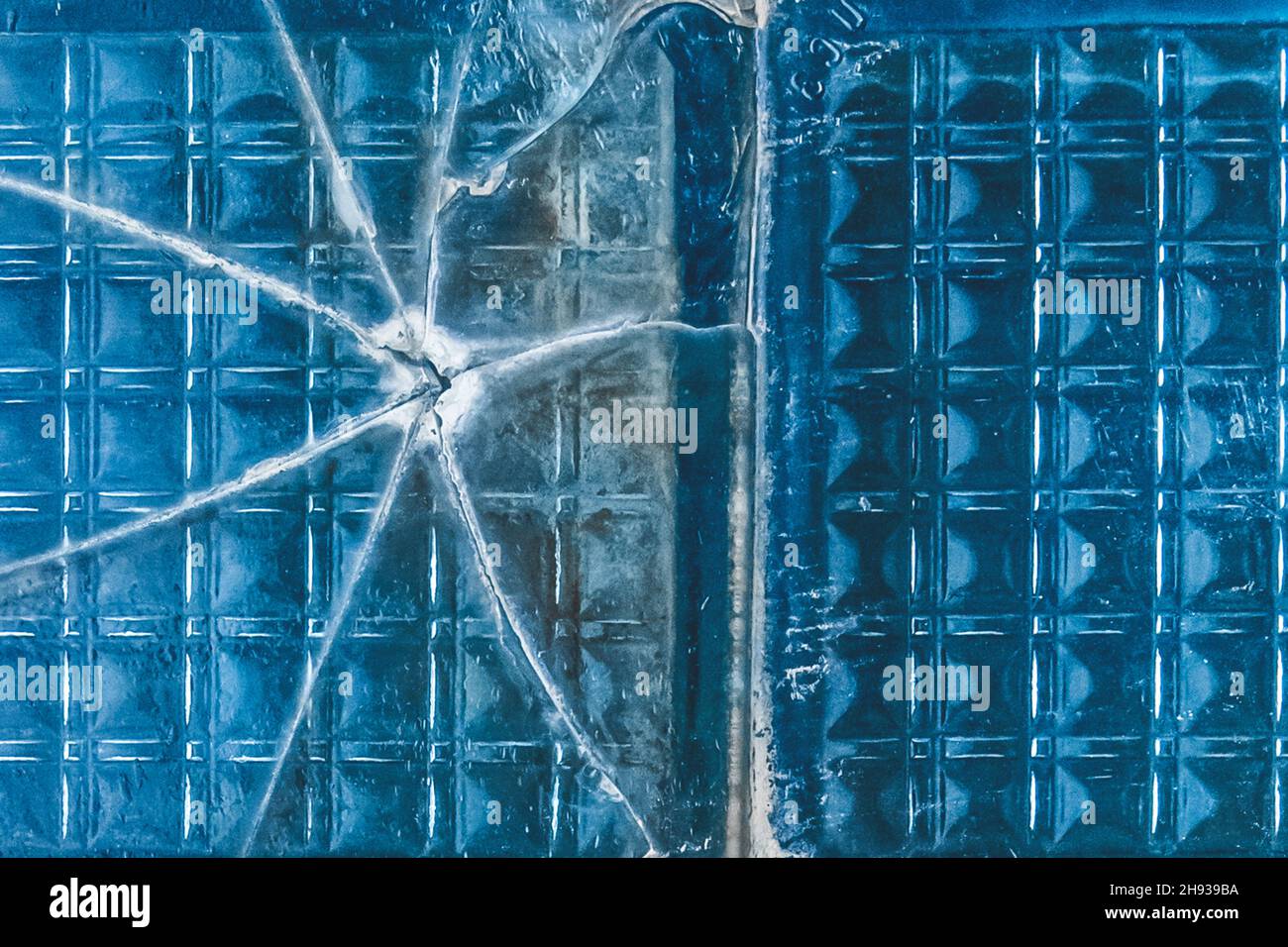 Old broken glass with cracks blue texture damaged background. Stock Photo