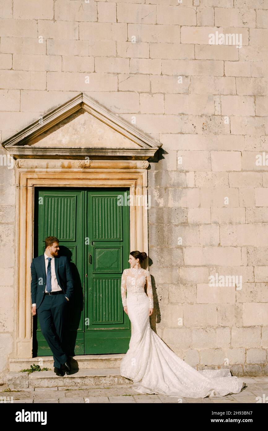 Groom and bride stand at the green door of the old stone house Stock ...