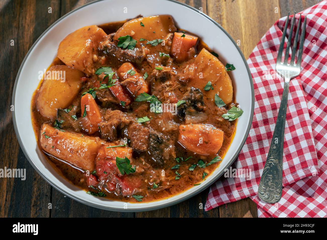Aerial view of a plate with meat stew, potatoes and vegetables on a wooden table Stock Photo