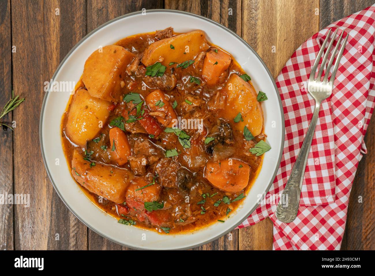 Aerial view of a plate with meat stew, potatoes and vegetables on a wooden table Stock Photo
