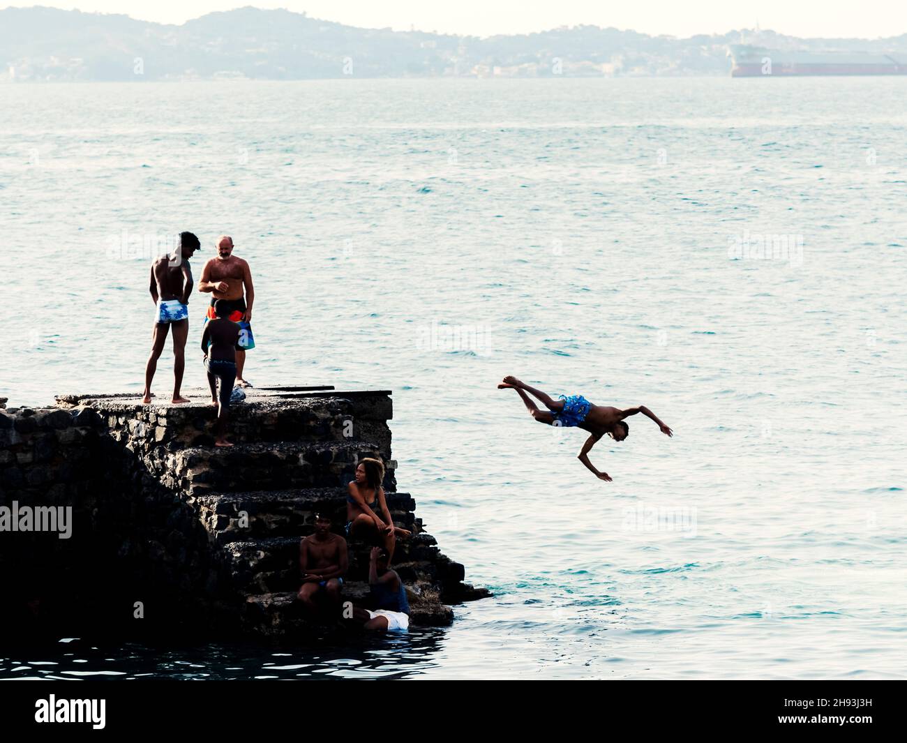 Young people jumping into the sea from the Fort of Santa Maria pier in Porto da Barra. Stock Photo