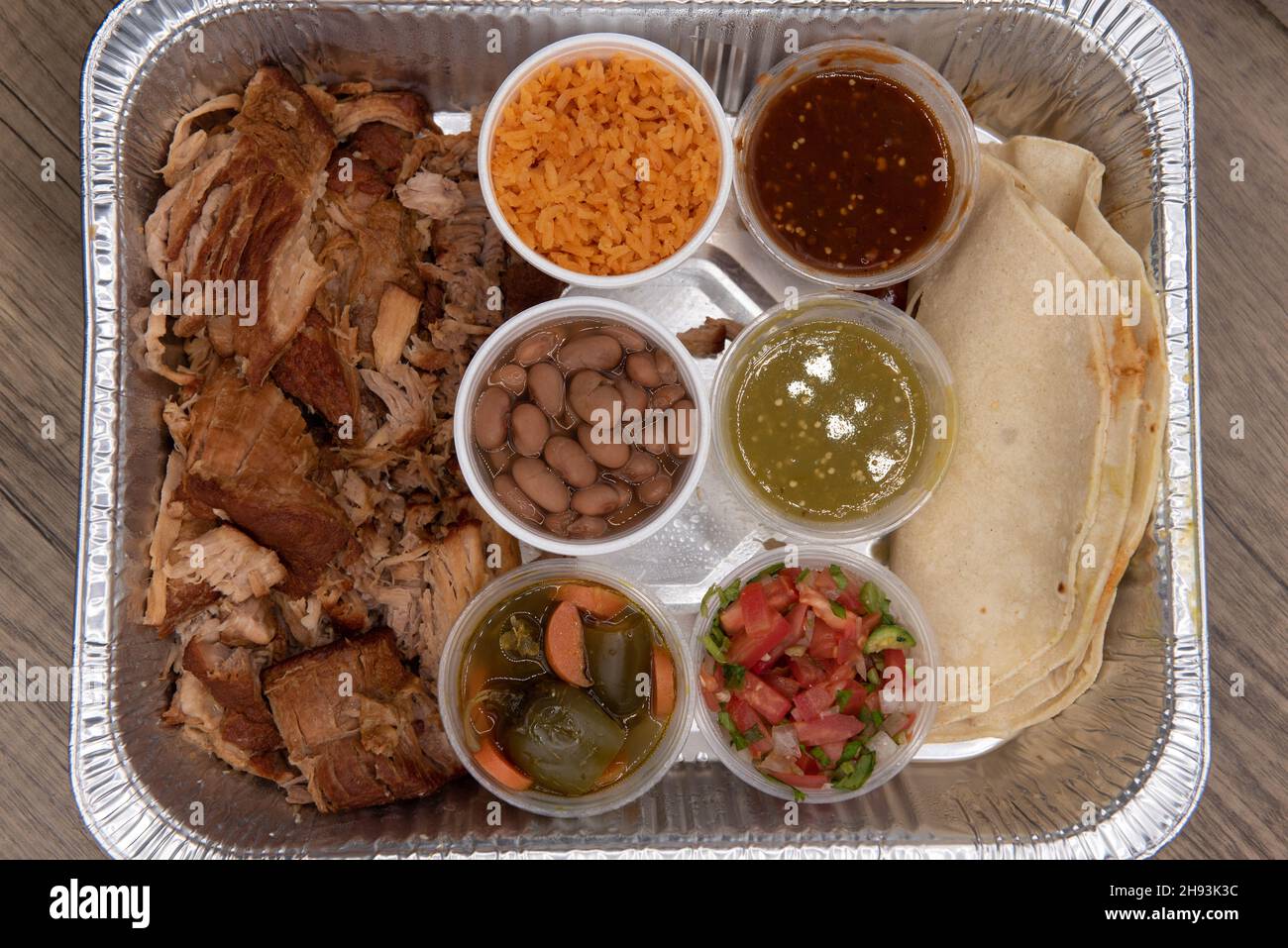 Overhead view of family sized portions of carnitas pork meat with rice, beans, and salsa to have tacos for everyone. Stock Photo