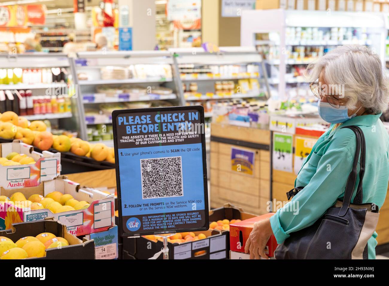 Australian grey haired lady wearing facemark and at check in before entry sign and QR code in Australia supermarket in Sydney during covid 19 pandemic Stock Photo