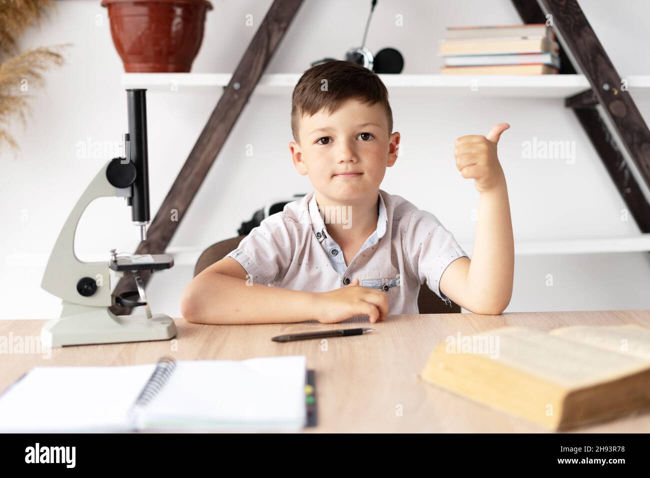 schoolboy boy studying at home at the desk has a biology lesson and a microscope. Online education and home tutoring. Pupil receives knowledge Stock Photo