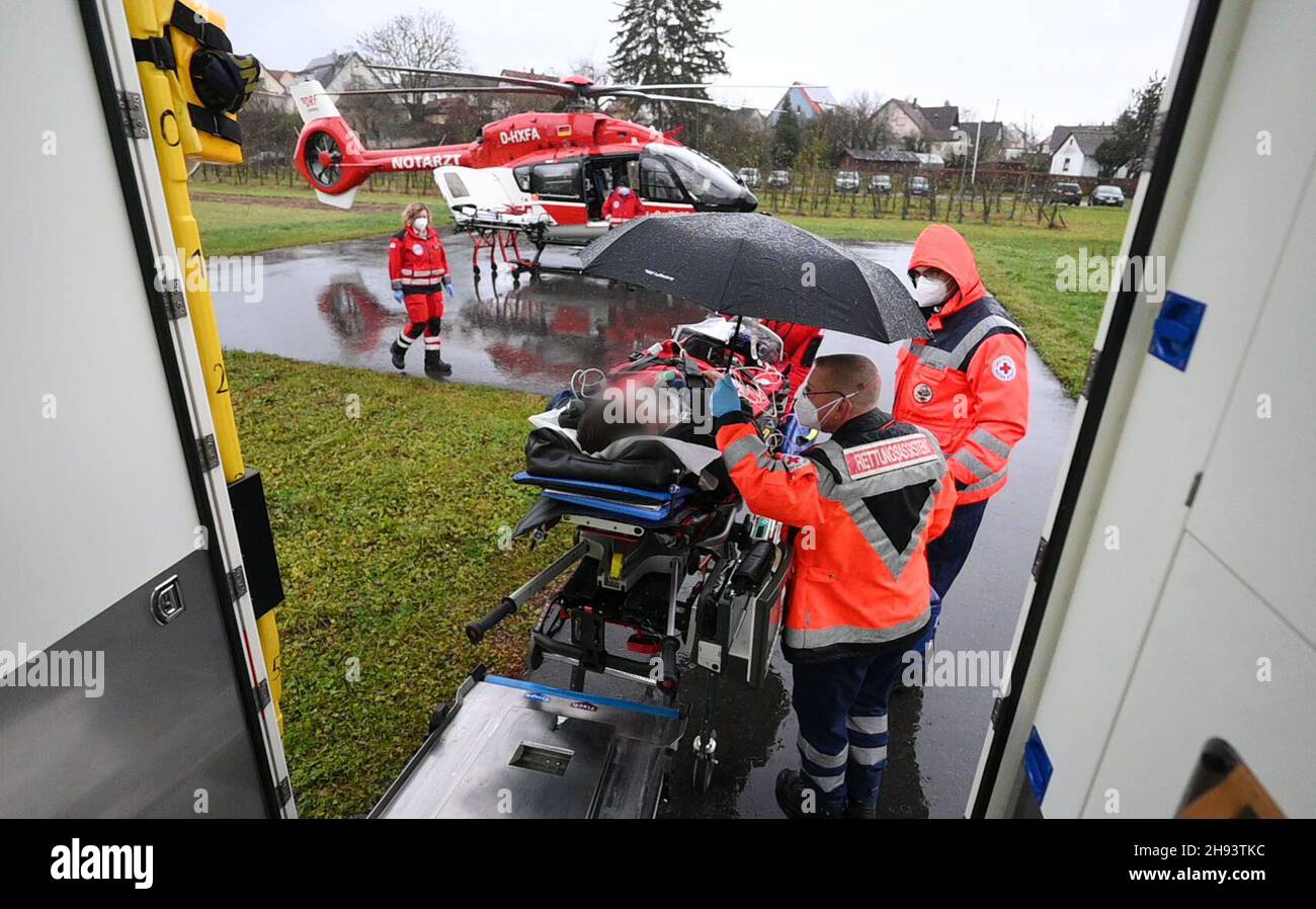 02 December 2021, Baden-Wuerttemberg, Öhringen: During a mission, a paramedic holds an umbrella over a patient who is being taken from an ambulance to the DRF rescue helicopter Christoph 51 for further transport. During the mission, the DRF transported a patient who did not have Covid-19 in the DRF rescue helicopter Christoph 51 from the intensive care unit of the Hohenlohe hospital to the intensive care unit of a rehabilitation clinic in Bavaria. Covid 19 patients are not the only ones who are now transported from one hospital to another by helicopter. In order to create capacity in the inten Stock Photo