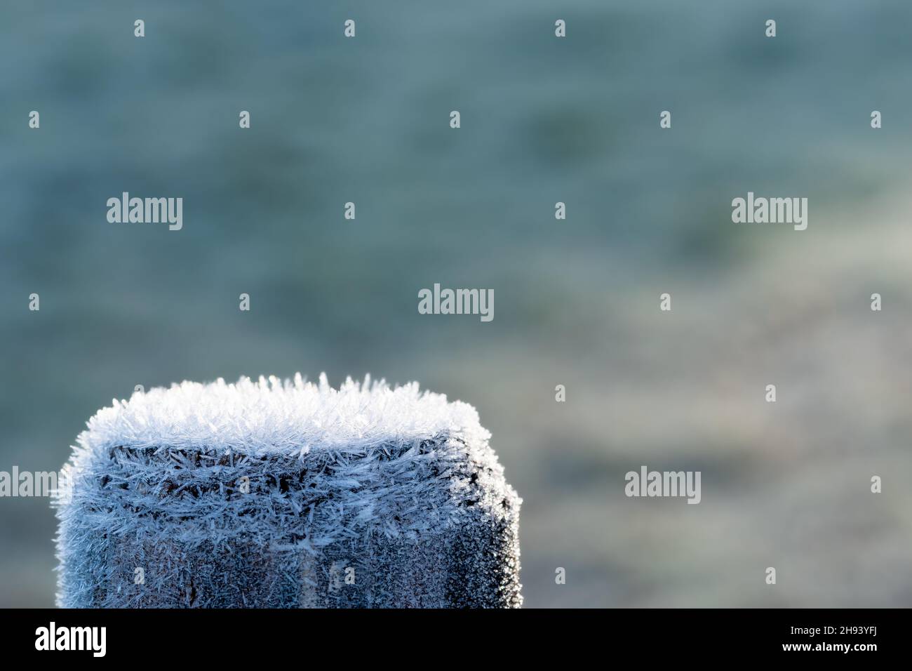 Top of a wooden fence pole covered with ice crystals, back-lit by morning sun. Concepts of frosty winter season, cold temperature, hoarfrost. Macro. Stock Photo
