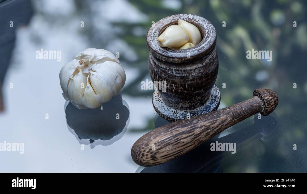 Fresh garlic with wooden mortar on modern glass table on nature background Stock Photo