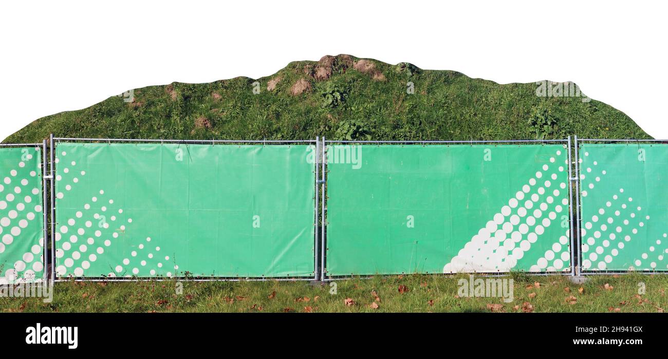 Behind the green fence of the construction site, a large pile of earth with grass. Isolated Stock Photo