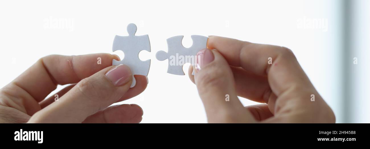 Female hands holding two white puzzle pieces closeup Stock Photo