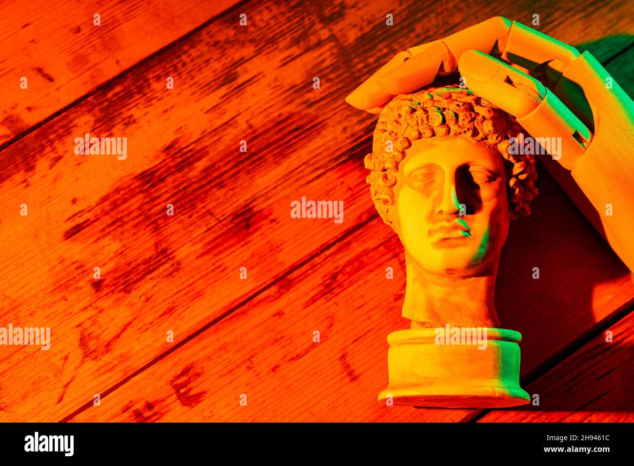 Ancient greek sculpture Hermes head and an artificial hand. Gypsum copy of ancient statue Hermes head in orange green neon light. Minimal art fantasy Stock Photo