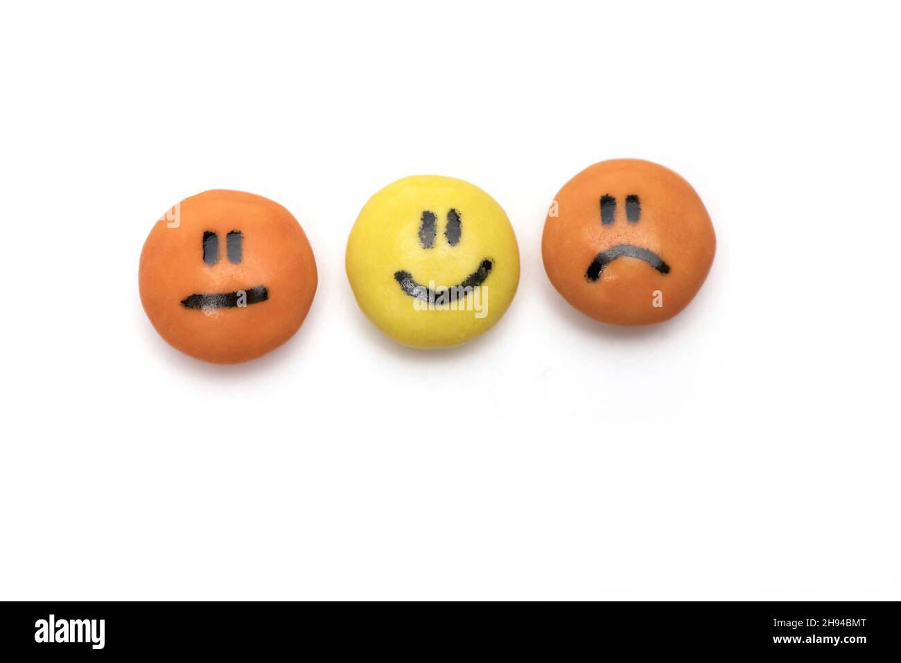 two orange and one yellow round candy with faces on them representing from sad to happy isolated on white background smileys Stock Photo
