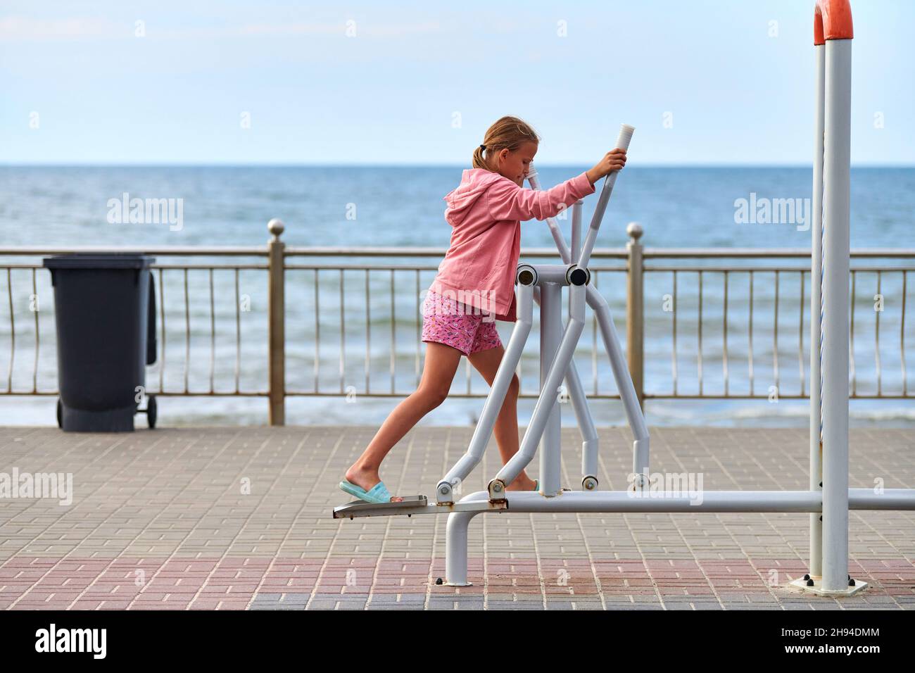 Zelenogradsk, Russia - 07.30.2021 - Young girl in pink clothes using air walker exercise machine, sea background. Girl engaged in fitness, footwork. O Stock Photo