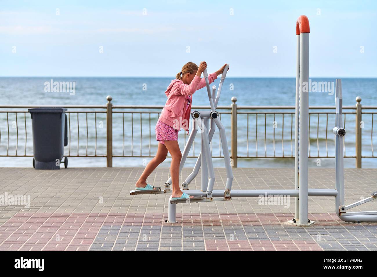 Zelenogradsk, Russia - 07.30.2021 - Young girl in pink clothes using air walker exercise machine, sea background. Girl engaged in fitness, footwork. O Stock Photo