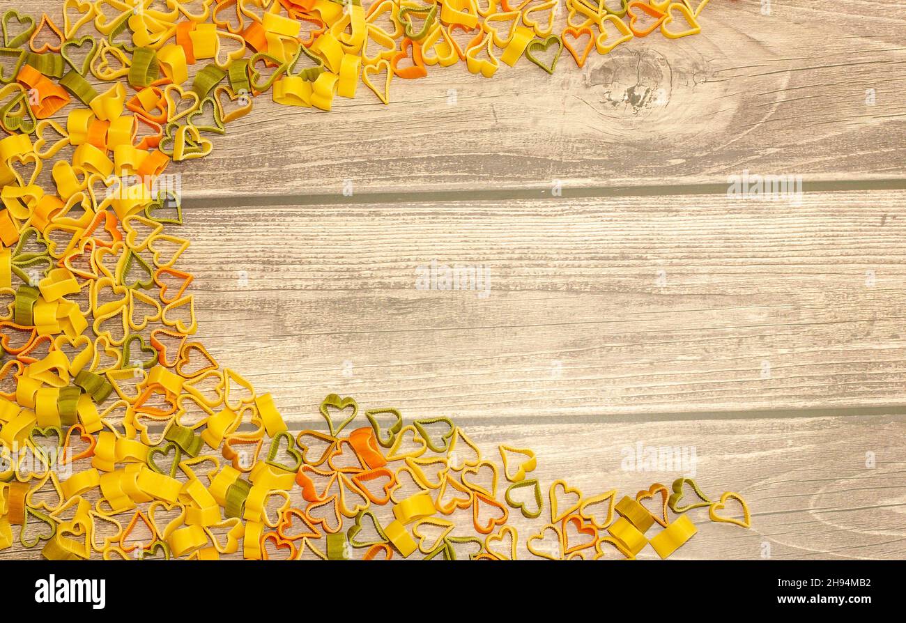 Frame of multicolored pasta in the shape of a heart on a wooden background, top view, copy space, selective focus Stock Photo