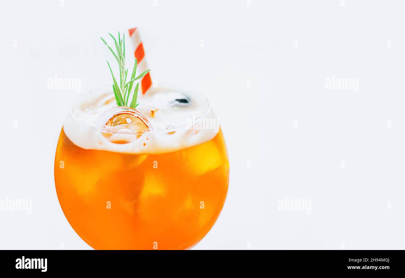 Close up glass of ice cold Aperol spritz cocktail decorated with rosemary and red striped straw served in a wine glass on white background. Stock Photo