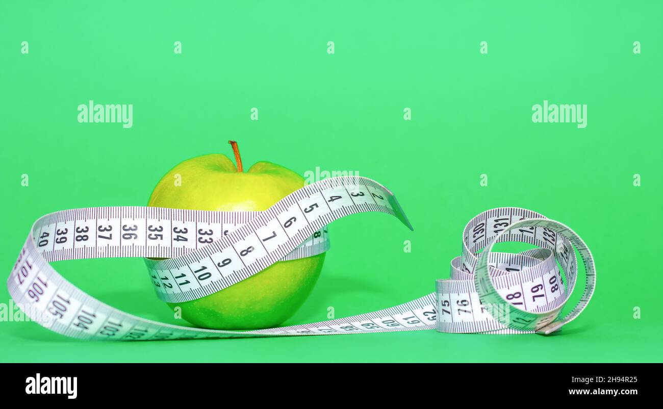green apple with gray tape measure on green background in healthy food and diet concept Stock Photo