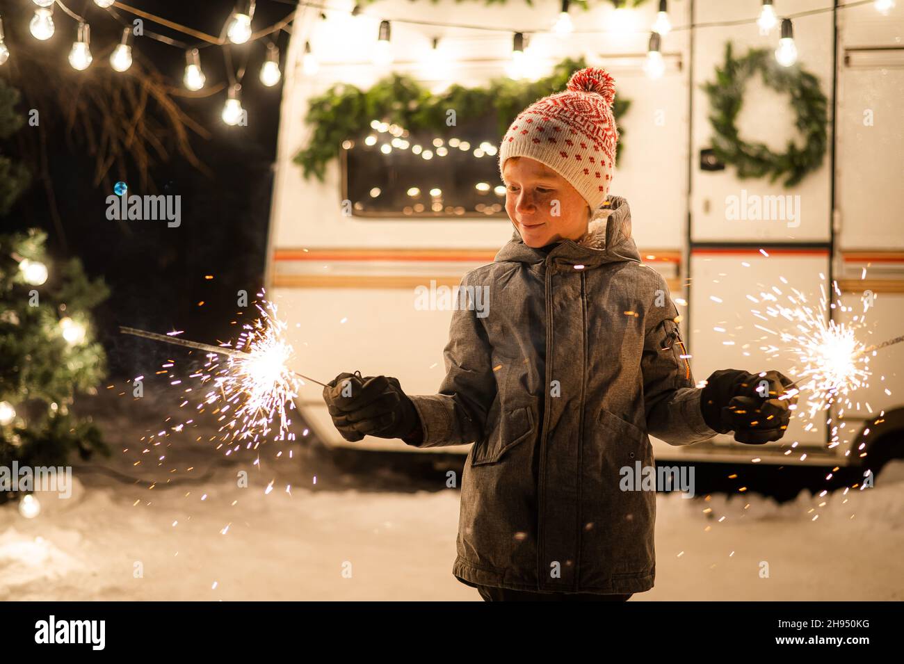 Caucasian red-haired boy holding sparklers by the trailer. Schoolboy celebrates Christmas on a trip. Stock Photo
