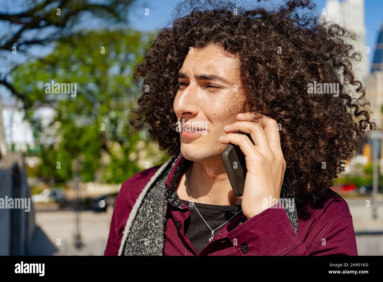 Close-up of a young curly-haired Latin man happily talking on the phone on a sunny day. normal view Stock Photo