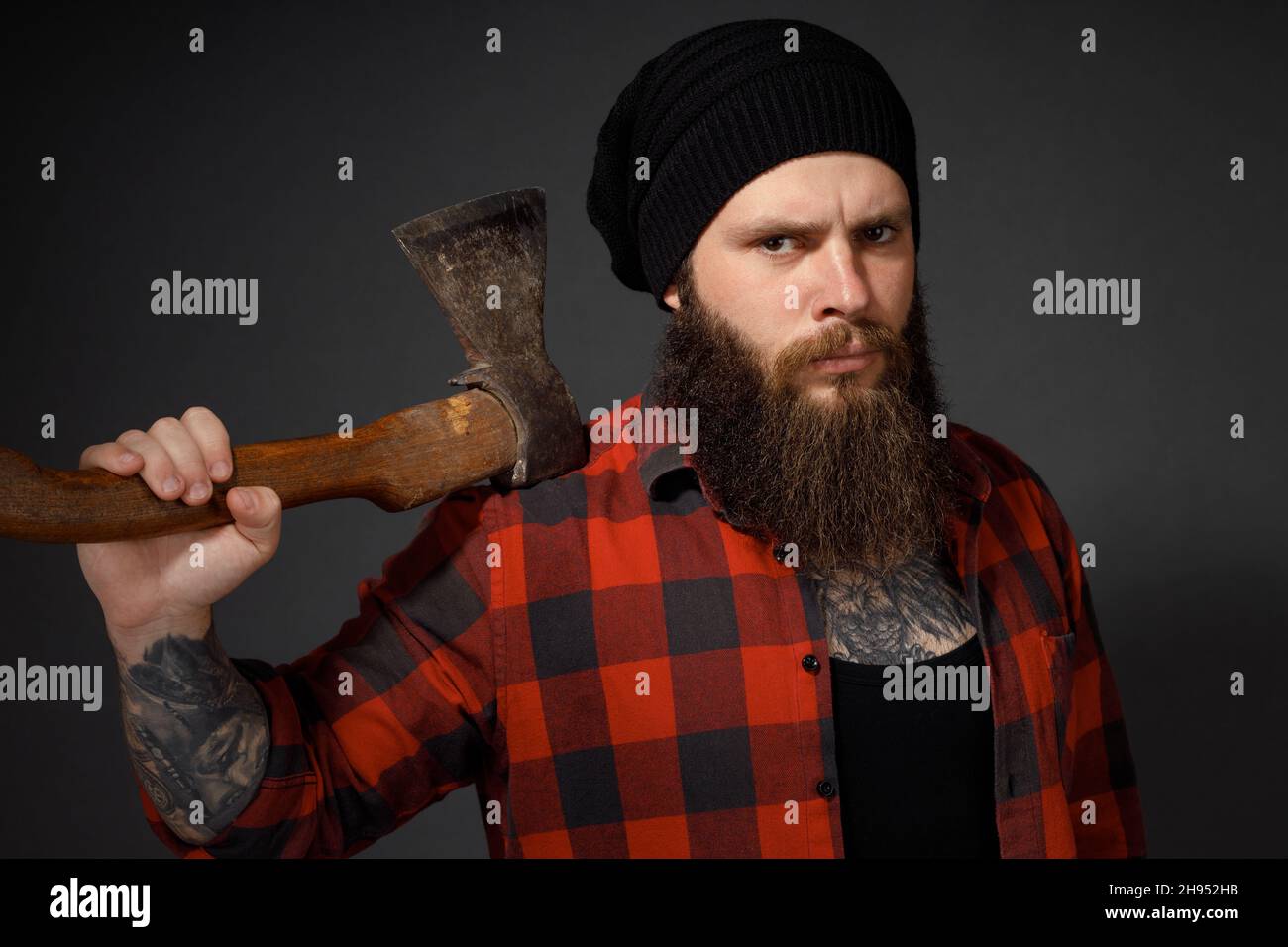 handsome man with long hair with an ax in his hands on a dark studio background. Stock Photo