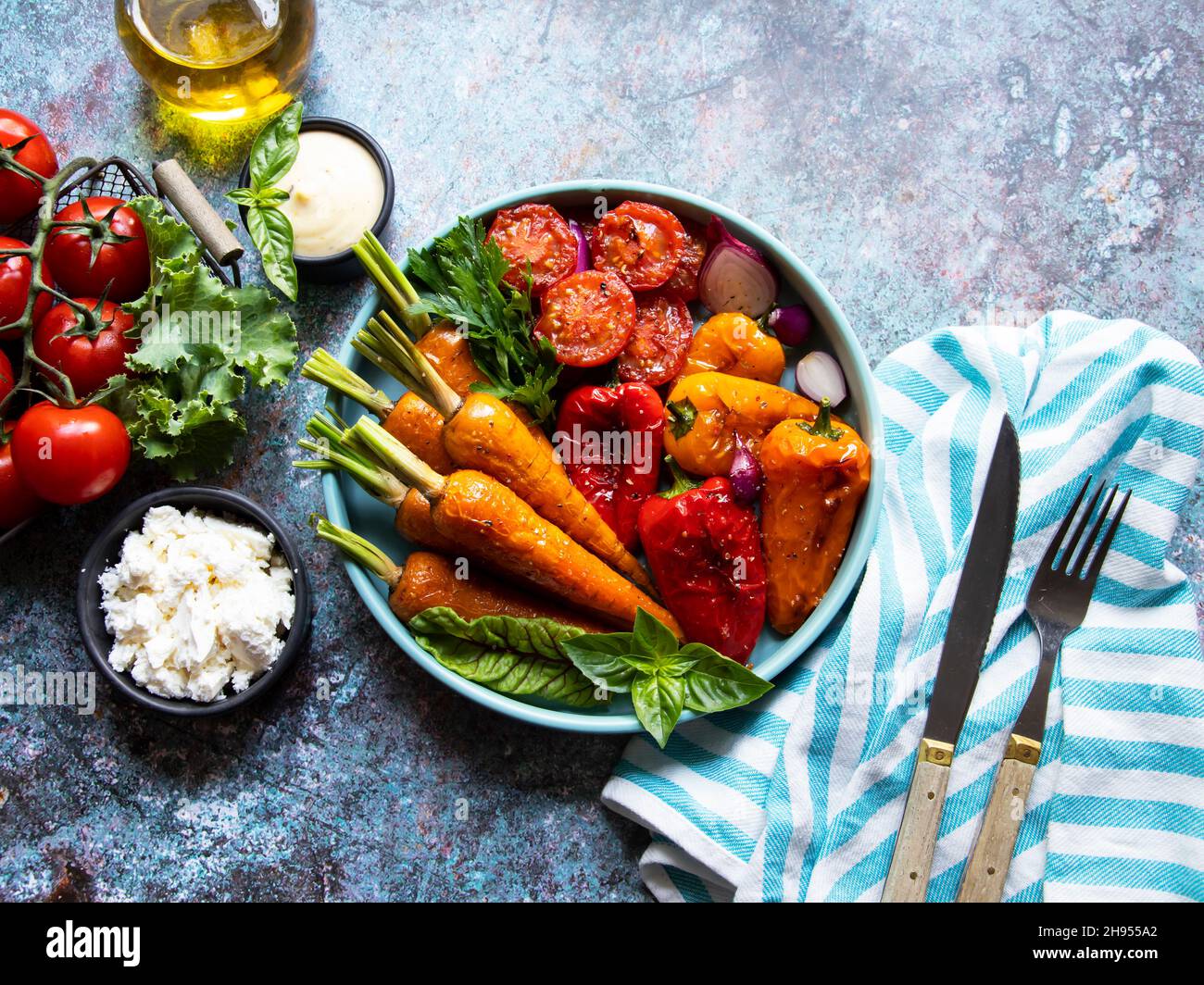 baked grill baby carrots, tomato, bell pepper in a plate, basil and spices vegan dish close up, white sauce Stock Photo