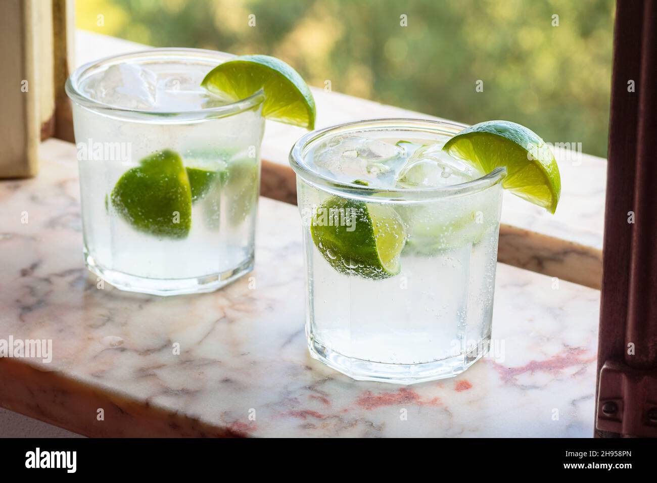 Gin and Tonic or Vodka and Soda Cocktail Drink with Limes and Ice in Marble Windowsill Stock Photo