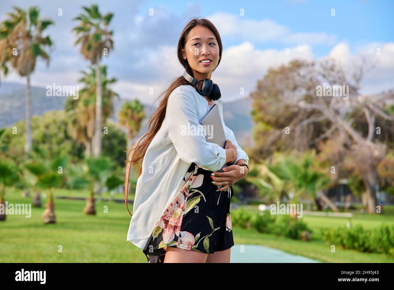 Portrait of young woman with backpack, headphones and laptop in her hands Stock Photo