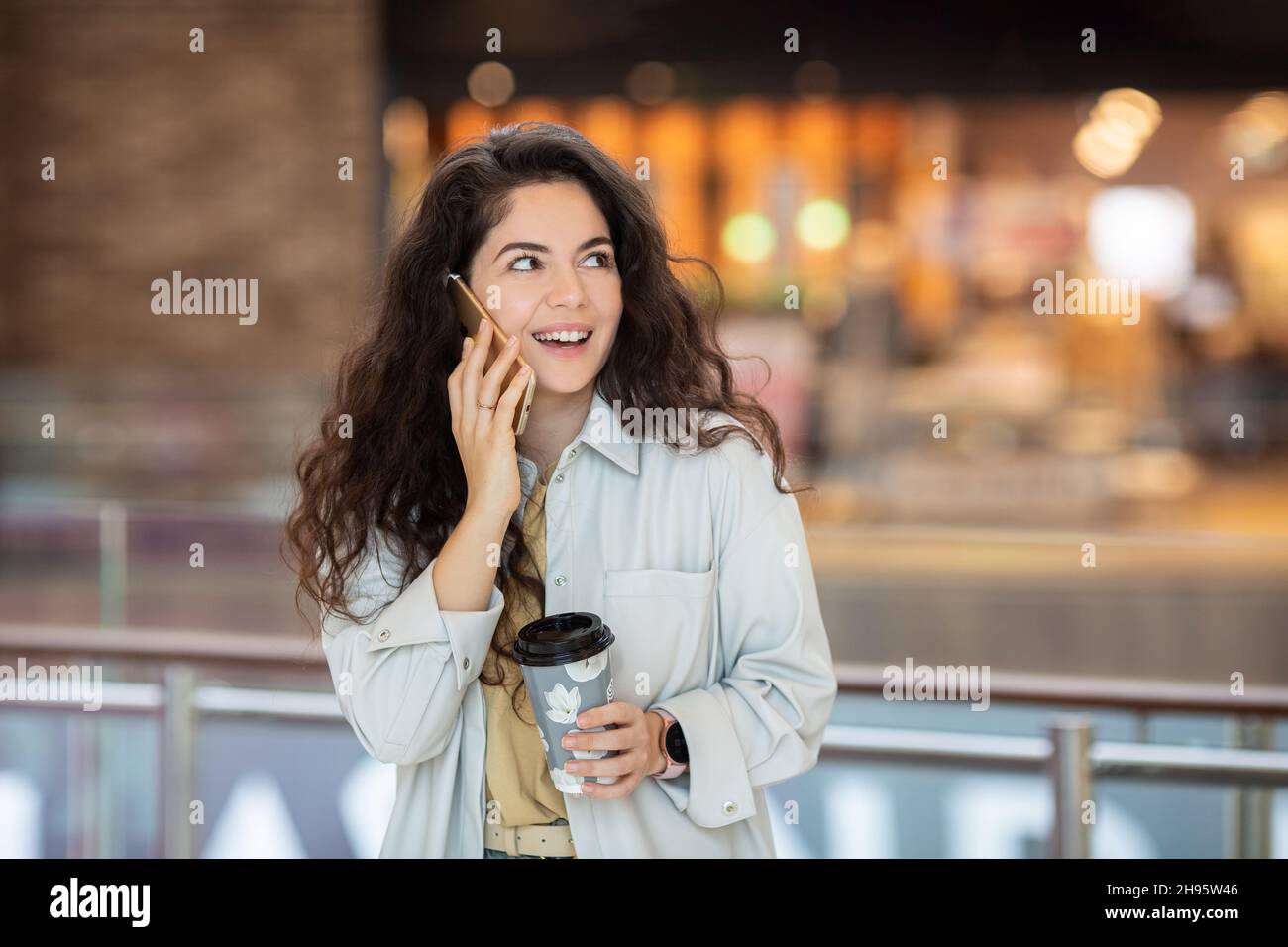 Young cheerfful woman using smartphone and drinking take away coffee in ...