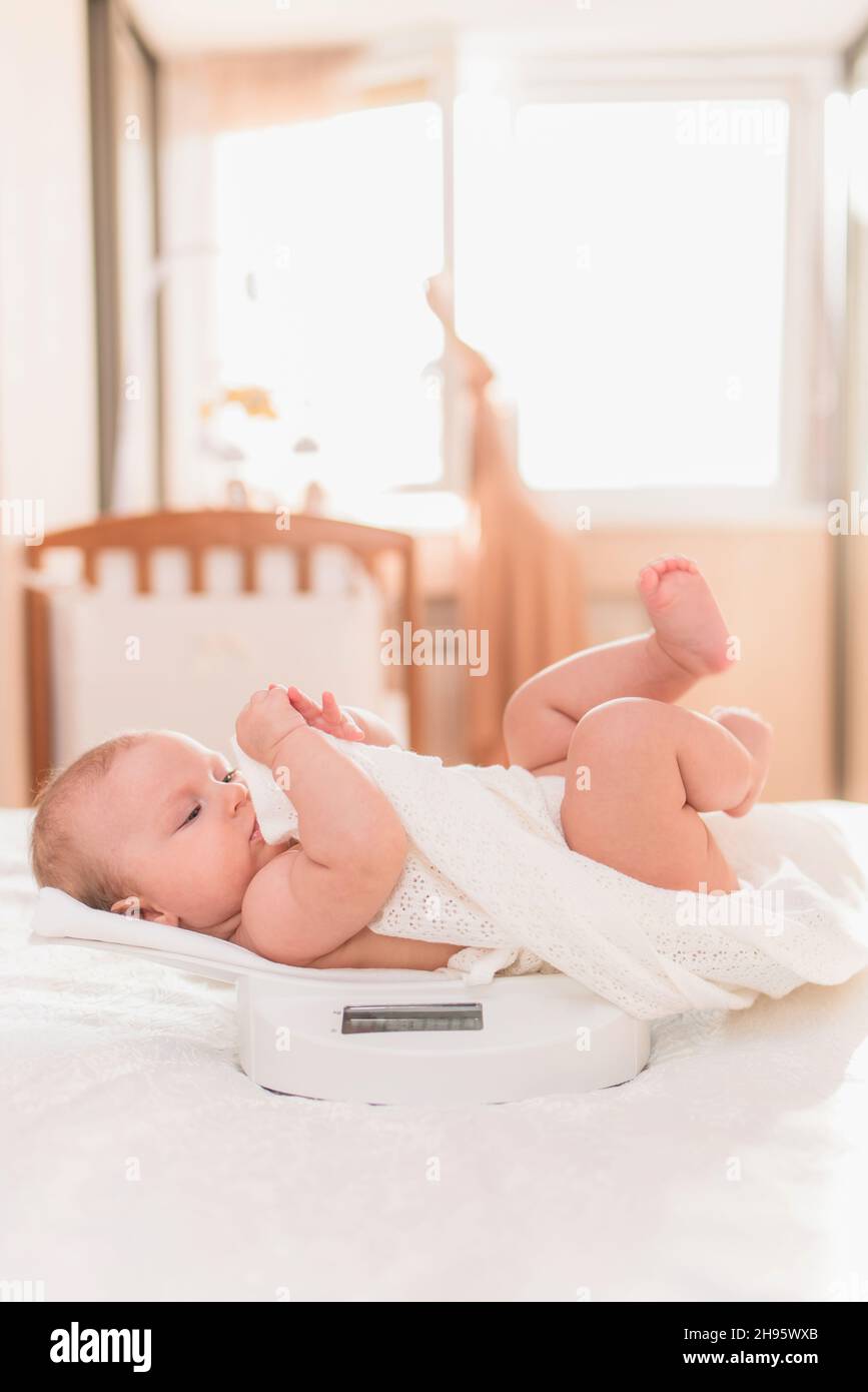 Happy baby is weighed on the scales in the bedroom Stock Photo