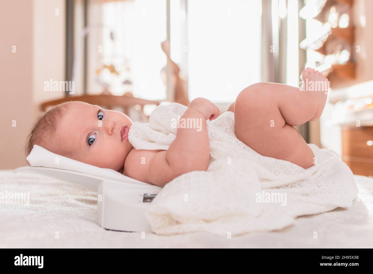 Beautiful newborn baby girl is weighed on the scales in the bedroom Stock Photo