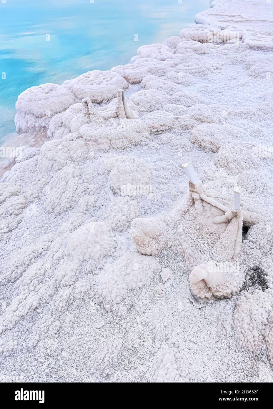 Small plastic chairs completely covered with crystalline salt on shore of dead sea, closeup detail, clear blue water near Stock Photo