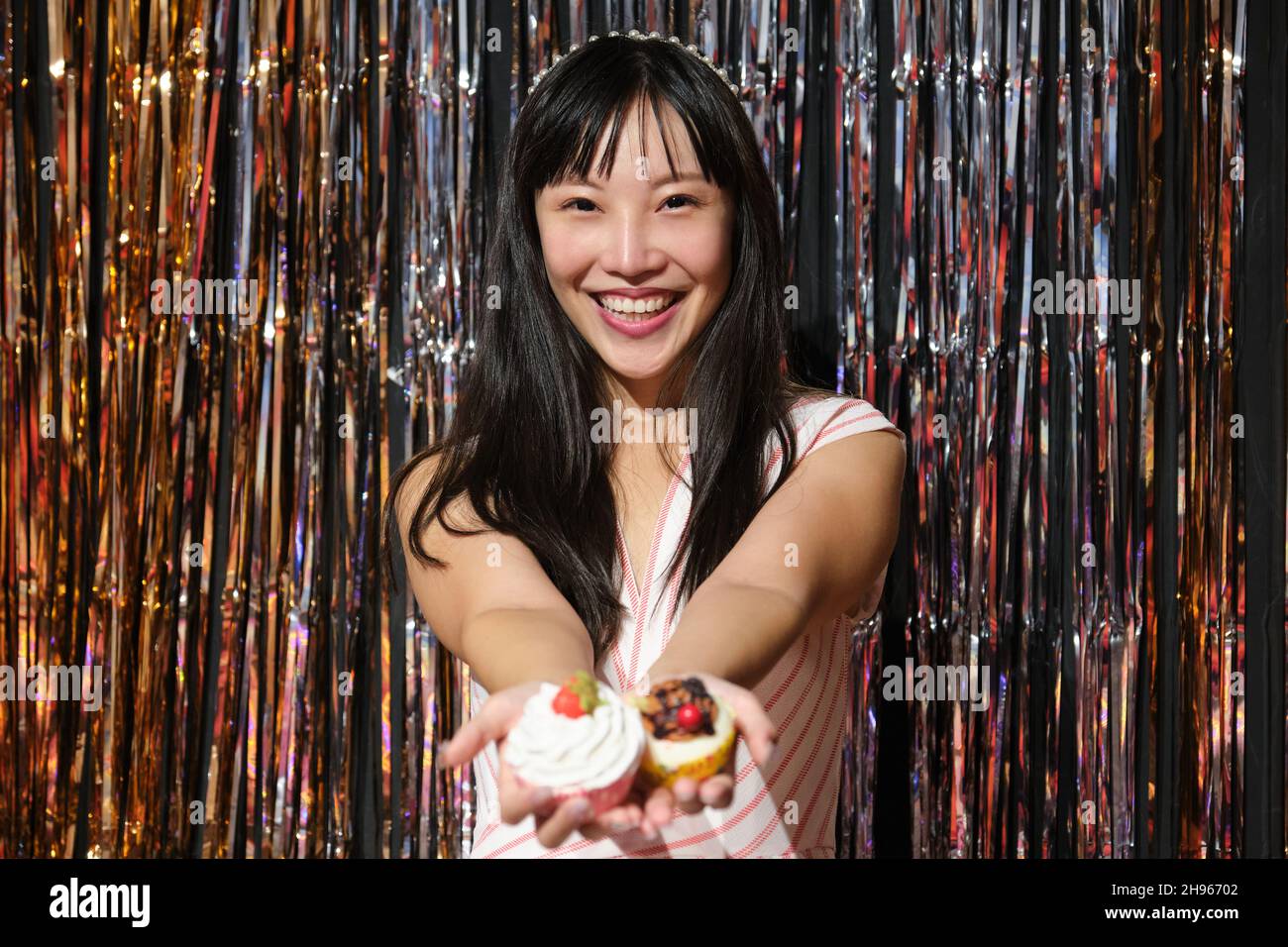 Young asian woman show cupcakes to the camera over a party background. Stock Photo