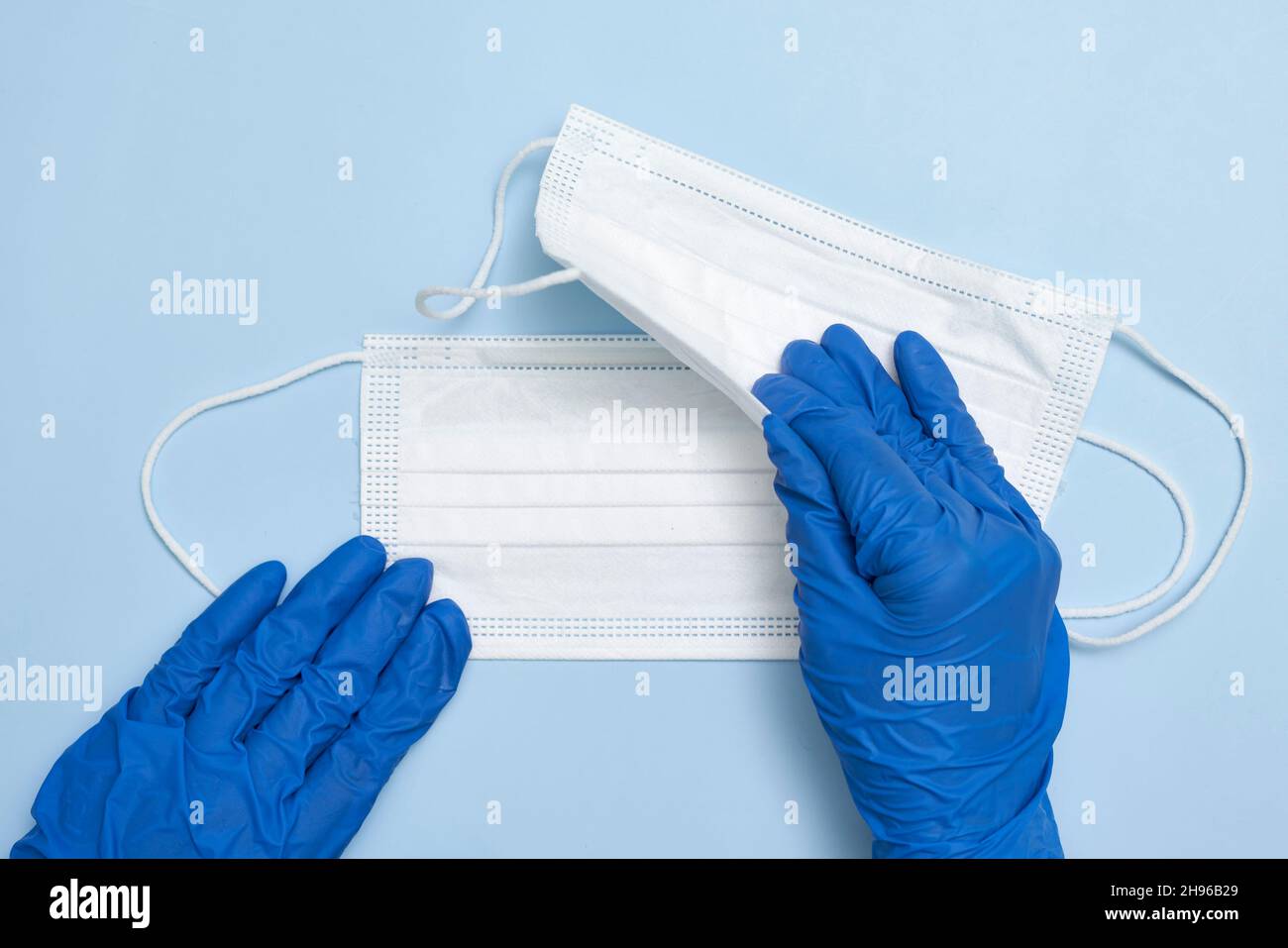 Hand in medical gloves holds two white medical face masks on blue background Stock Photo