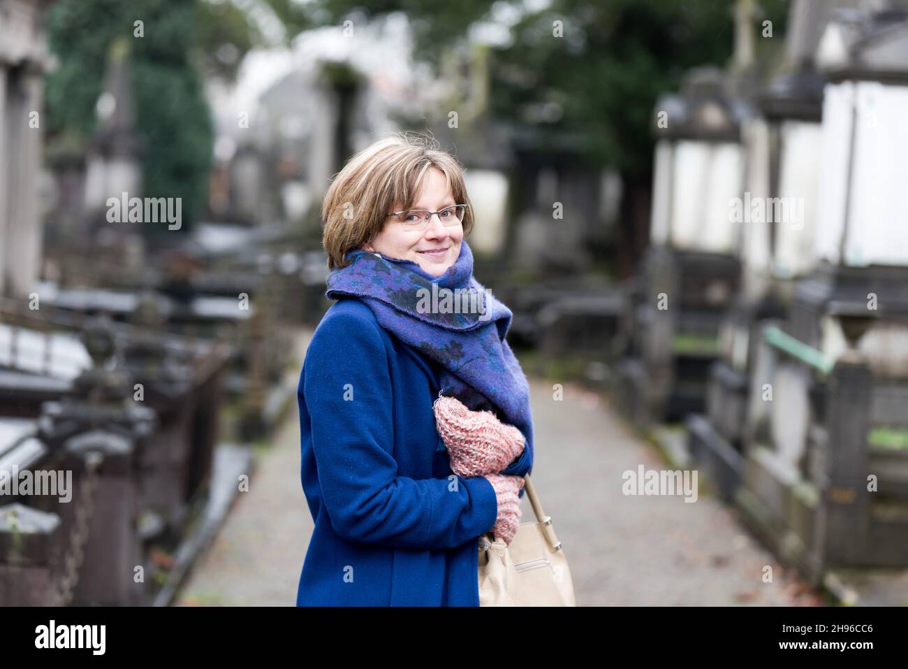 Portrait of a thirty year old woman with a blue winter coat and scarf at a cemetery Stock Photo