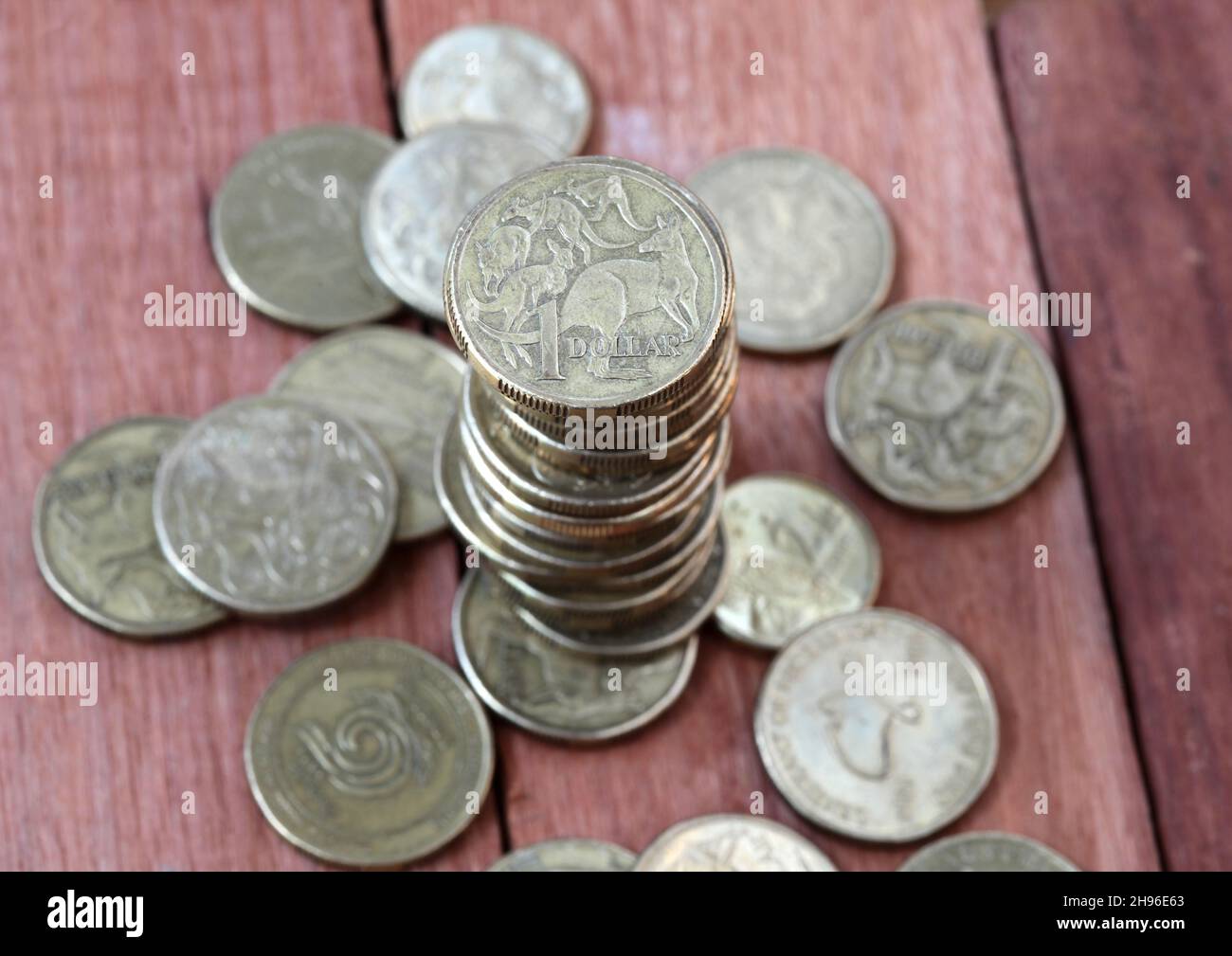 A pile of Australian one dollar coins on a wooden background. Shallow depth of field, focus on coin at top of pile. Stock Photo