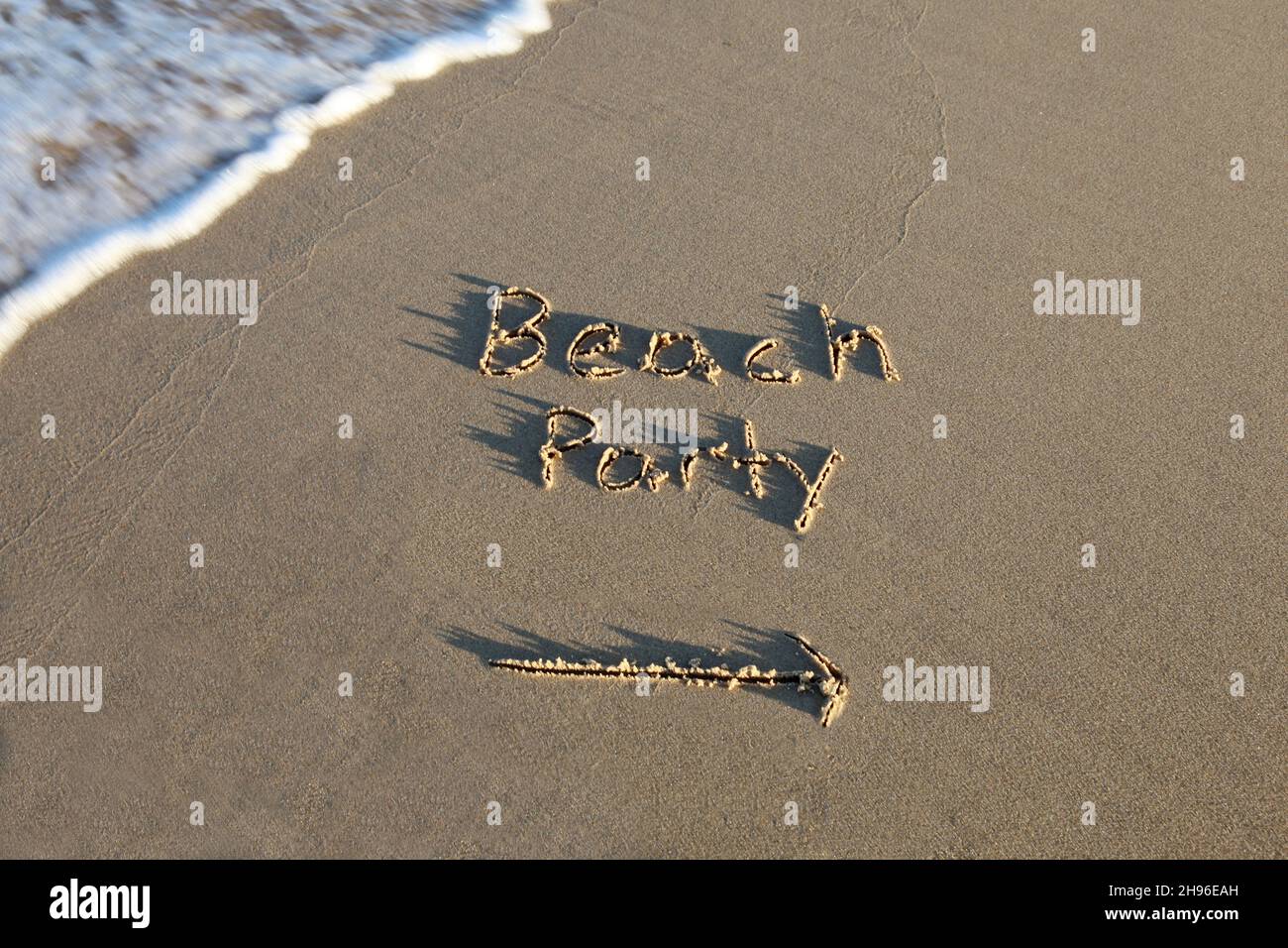 Beach party written in the sand at the beach. The arrow points the way. Wave with motion blur. Stock Photo