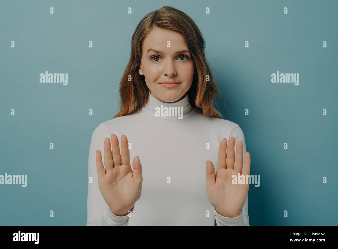 Attractive young focused woman showing stop gesture, saying no, isolated over blue studio background Stock Photo